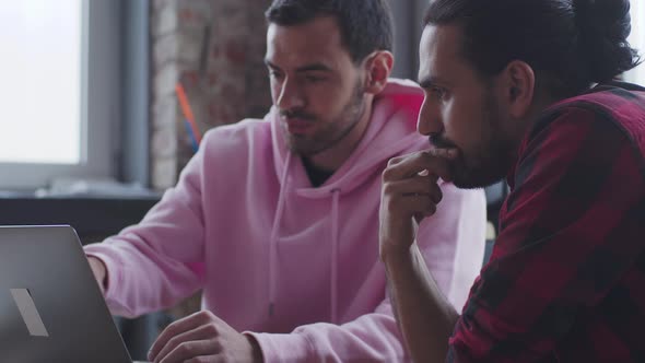 A Young Businessman with a Laptop Talks to a Colleague in the Office