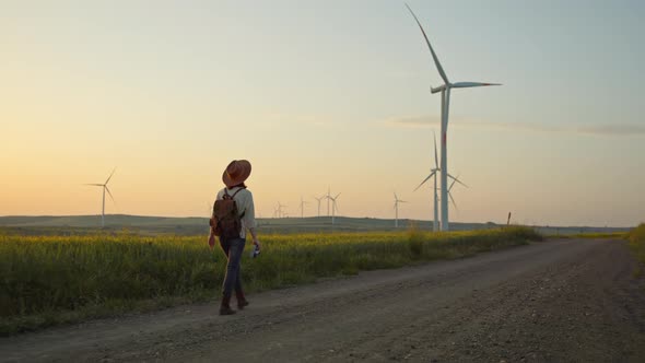 Attractive hiker with a camera walking near a farm with alternative green energy windmills