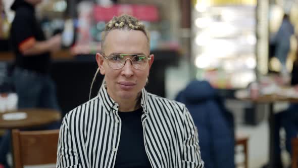 A Cute Stylish Homosexual Man in a Shopping Center Cafe is Sitting at a Table with a Glass of Coffee