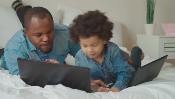 Positive Father and Son Working on Laptop on Bed