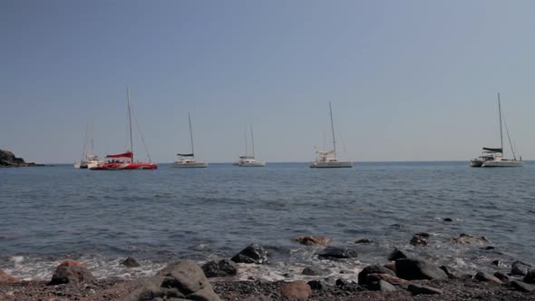 Catamarans by a rocky beach. Black Volcanics rocks in the foreground of this tracking shot.