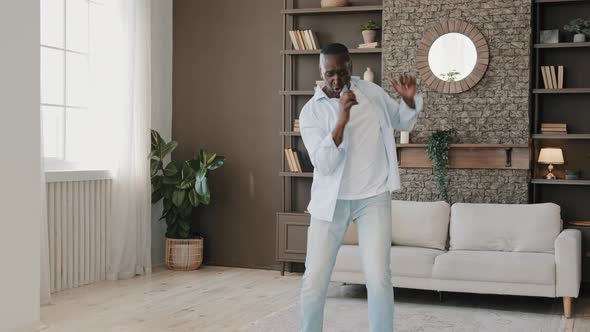 Senior African American Comical Adult Man Active Moving Dancing in Modern Living Room Singing Loud