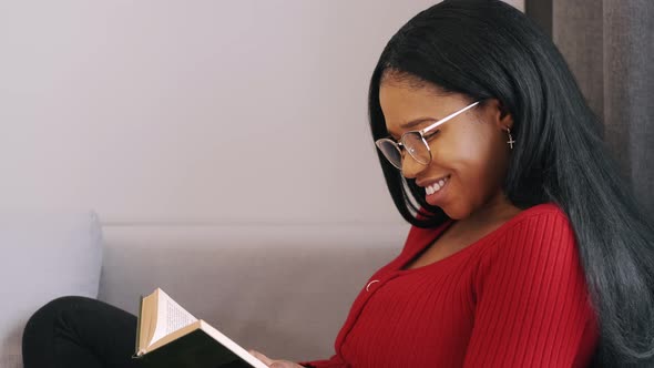 African American Woman Reading a Book Sitting on Bed at Home