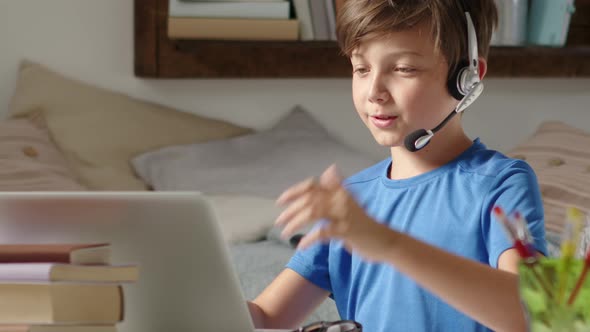 smiling student boy studying at home with remote school connected to computer on the web