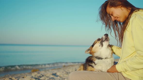 Candid Laughing Latin Girl in Yellow Hoodie at Summer Beach with Cute Pet Corgi Dog Sitting in Front