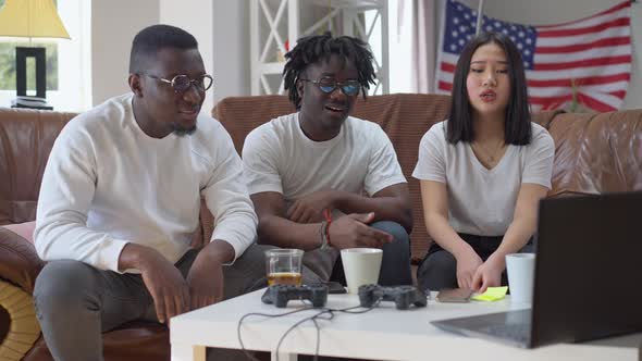 Absorbed Multiethnic Friends Watching Match on Laptop Making Disappointed Facial Expression Talking