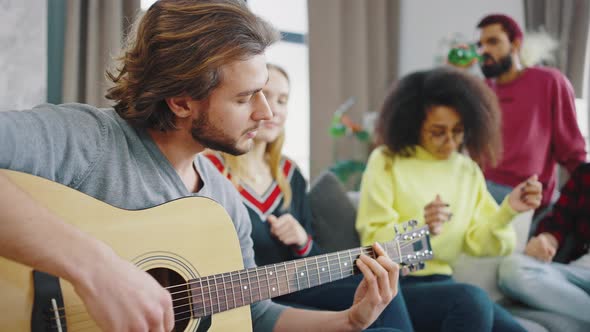 Caucasian Guy Playing Acoustic Guitar in the Company of Mixed Race Friends of Students