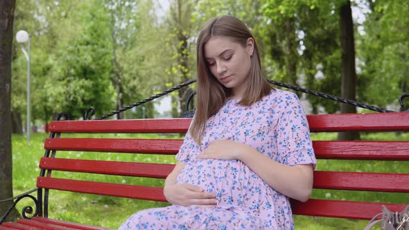 A Pregnant Woman Sitting on the Street in Summer and Holds Her Hands on Her Belly