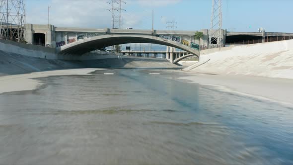 Drone Flying Fast Above Blue Los Angeles River Through Cinematic Concrete Bridge