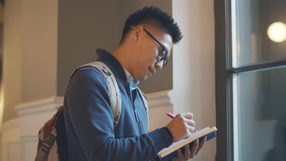 Side View of Asian University Student Writing Notes Standing in Corridor