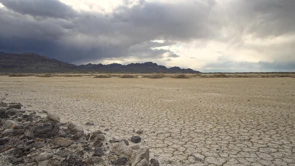 Panning over rocks and dry cracked desert in viewing dark clouds