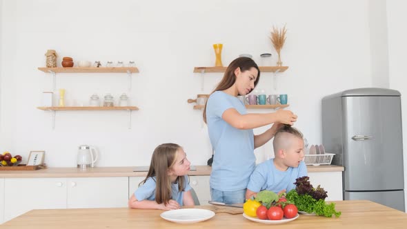 Young Mother Braids Her Son's Hair While Sitting in the Kitchen