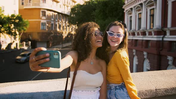 Two Young Ladies in Sunglasses are Laughing While Taking Selfie on Cell Phone