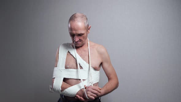 Senior Man with Bandage Examines Broken Shoulder at Wall