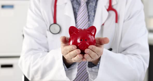 Man Doctor Holding Red Piggy Bank in Clinic Closeup  Movie Slow Motion