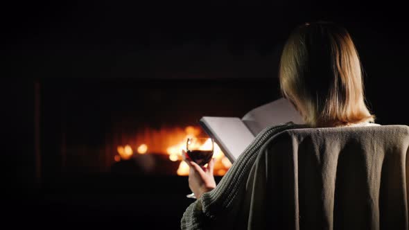 Woman with a Book and a Glass of Wine is Relaxing at Home By the Fireplace