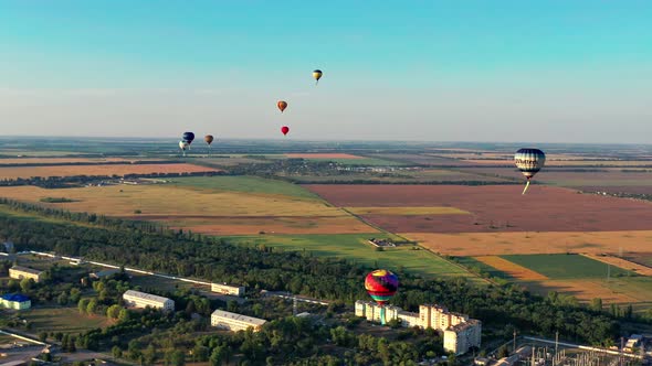 Multicolored balloons fly over fields, houses, trees. Blue sky.