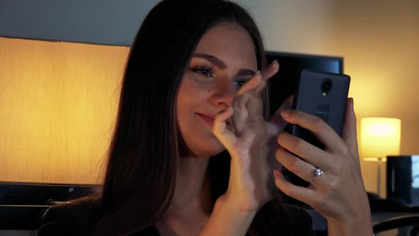 A Young Beautiful Woman Works on a Smartphone in a Dimly Lit Room - Closeup