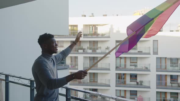 Happy Young Black Man Waving Rainbow Flag From the Balcony