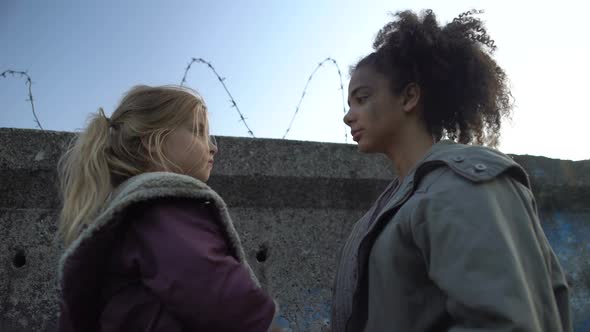 Mixed-Race Teenage Friends Embracing Looking at Barbed Wire Fence, Refugee Camp