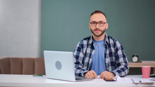 Portrait of Handsome Guy in Glasses Posing at Table in Front of Laptop