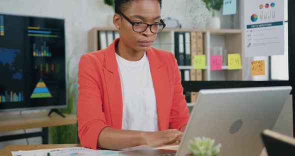 Focused young african woman working on laptop while sitting at workplace