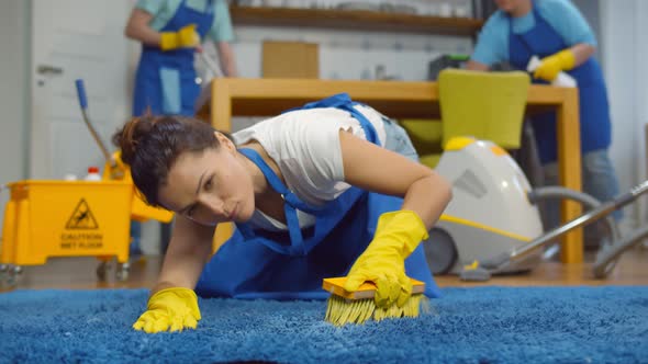 Woman Using Brush and Detergent for Floor Cleaning with Her Team in Living Room