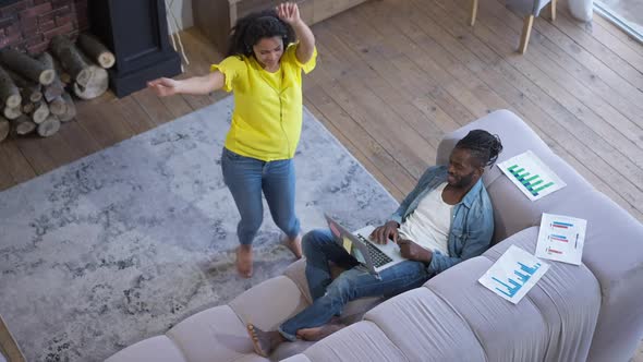 High Angle View of Happy Joyful African American Wife in Headphones Dancing in Living Room As