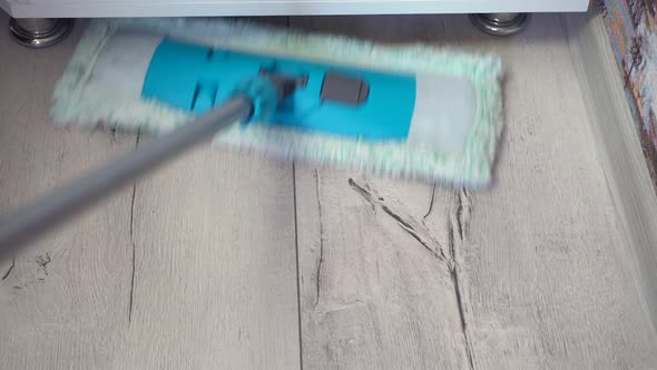 Man Cleaning Floors with Mop on Gray Laminate Surface Next to Cupboard and Plinth Wall