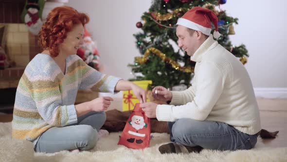 Side View Portrait of Happy Adult Couple Putting Candies in Christmas Sock and Talking