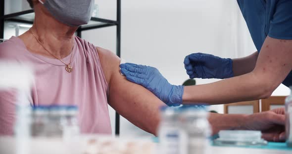 Doctor in Blue Scrubs Medical Gloves Gives Vaccine Injection Shot with Hypodermic Needle to Senior