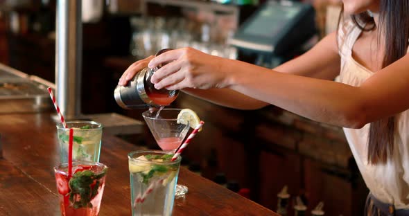 Barmaid pouring cocktail in glass at bar counter