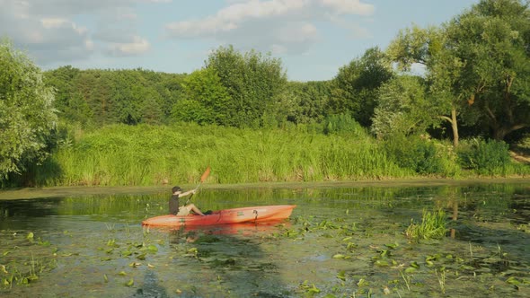 Fitness muscular man is sailing in kayak on river at sunset. Sport rowing.