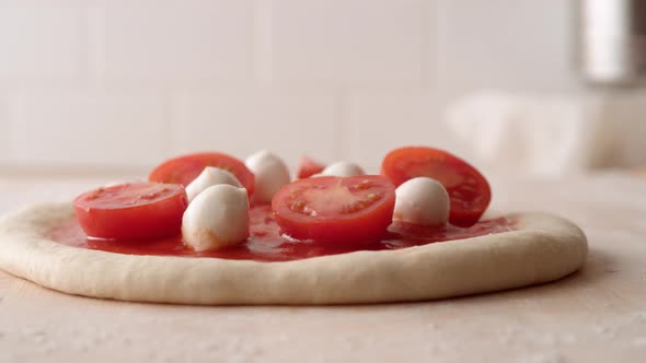 Camera follows putting a fresh basil leaf on a pizza dough. Slow Motion.