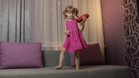 Child Girl with Wireless Speaker Enjoying Listen Music. Dancing on Sofa at Home