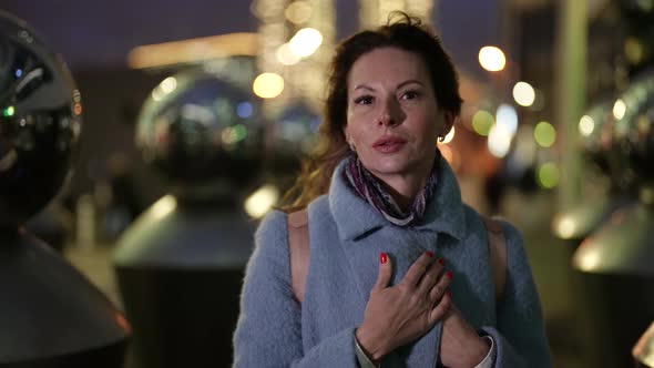 Portrait of a Woman in a Light Coat and with Colorful Nails Against a Background of Blurred Metal