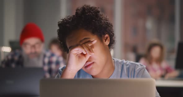 Exhausted Africanamerican Woman Rubbing Temples While Working Late at Night in Dark Office