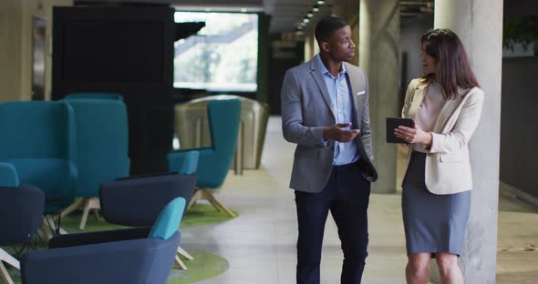 Diverse businessman and businesswoman discussing and using tablet in modern office