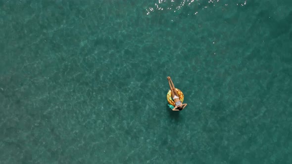 Aerial Top View of Turquoise Sea Water and Woman Swimming on the Yellow Swim Ring