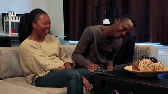 Young Black Happy Couple Watch Television in Living Room and Laugh