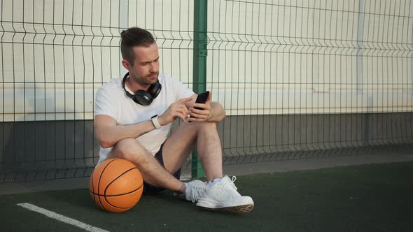 Man Relaxing After Basketball Training and Searching Music on Smartphone