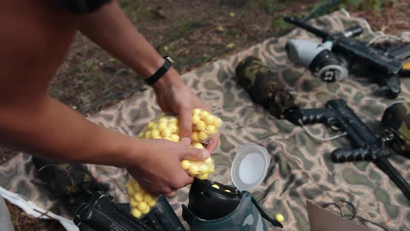 Men's Hands Pour Yellow Paintball Balls Into Weapon Tank