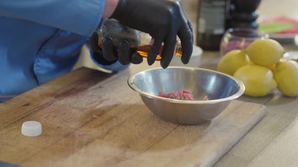 Hands of Professional Cook in Black Rubber Gloves Pouring Oil From the Bottle in the Aluminum Bowl