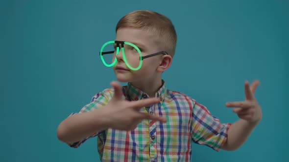 Preschool Boy Wearing Neon Eyeglasses Dancing on Blue Background in Slow Motion