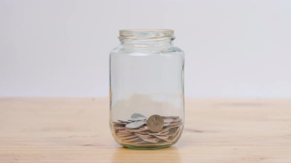 Stop motion animation coin into a clear glass jar on wooden desk. Savings and Investments concept.