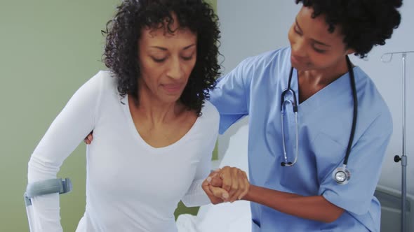 Front view of African american female doctor helping female patient to walk in the ward at hospital