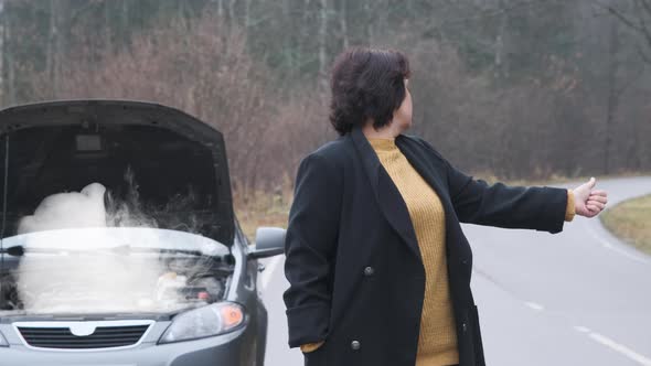 A Woman Stands By the Road Near a Broken Car