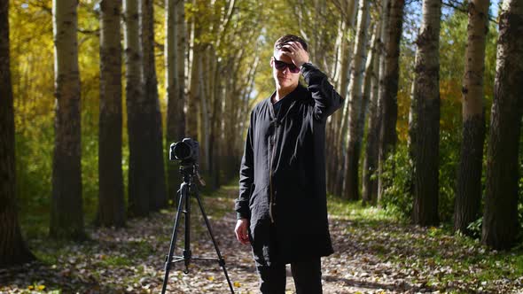 the Photographer Stands Near the Tripod and Puts on His Glasses in Park
