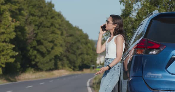 Young Frustrated Woman Talking on Mobile Phone, Leaning at Her Car with Warning Signals on