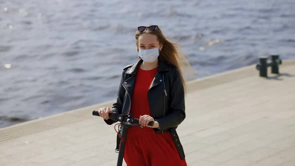 Young Blonde Woman in Surgical Mask with Electric Scooter